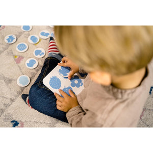 Enfant qui associe les jetons bleus sur la planche du jeu Nathan Couleurs et formes