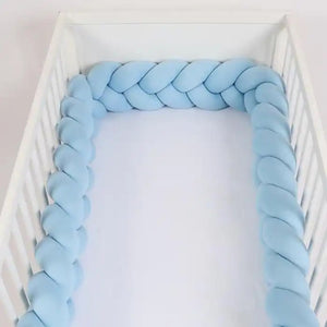 Tour de lit tressé bleu ciel installé tout autour d'un lit à barreaux blanc