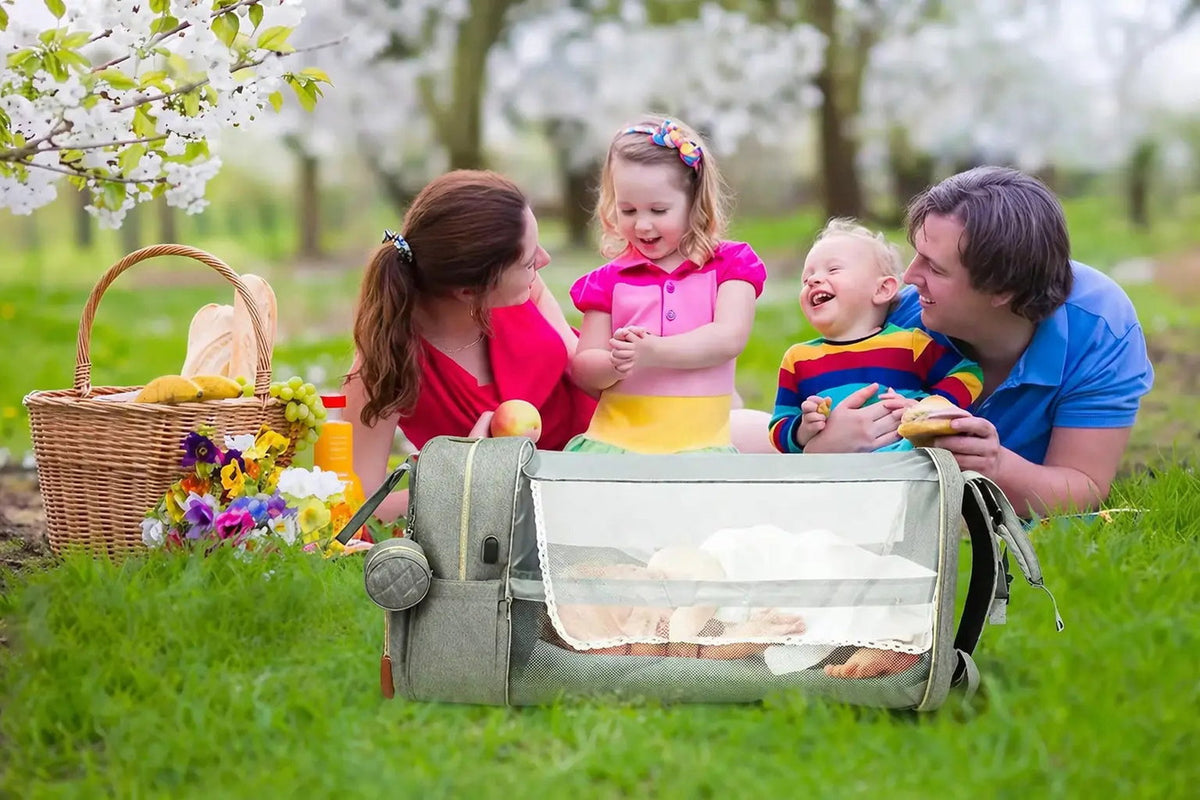 Famille en pique-nique avec le sac à langer déplié en lit d'appoint sur l'herbe