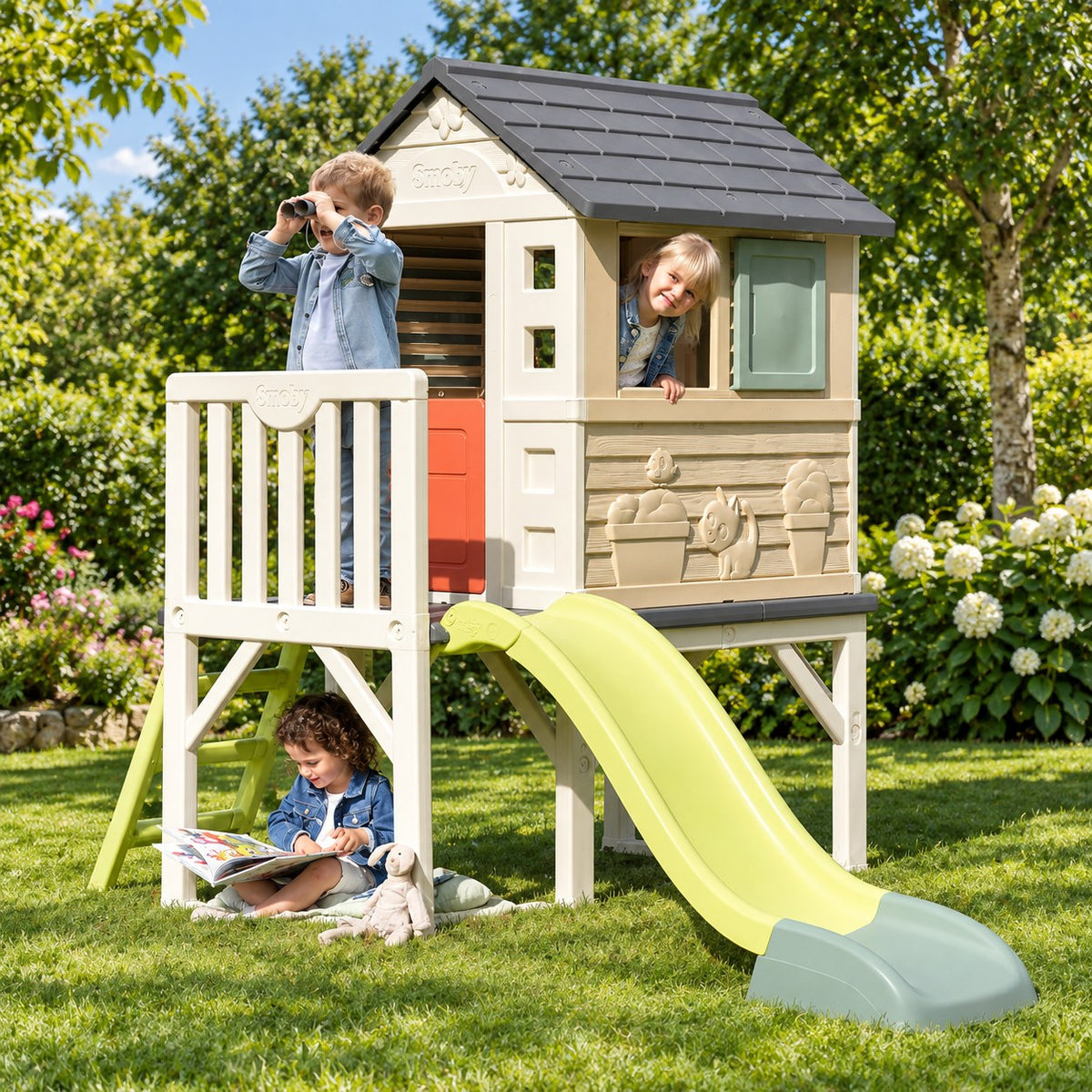 Enfants jouant sur la terrasse et à l'intérieur de la Maison Pilotis Smoby dans un jardin